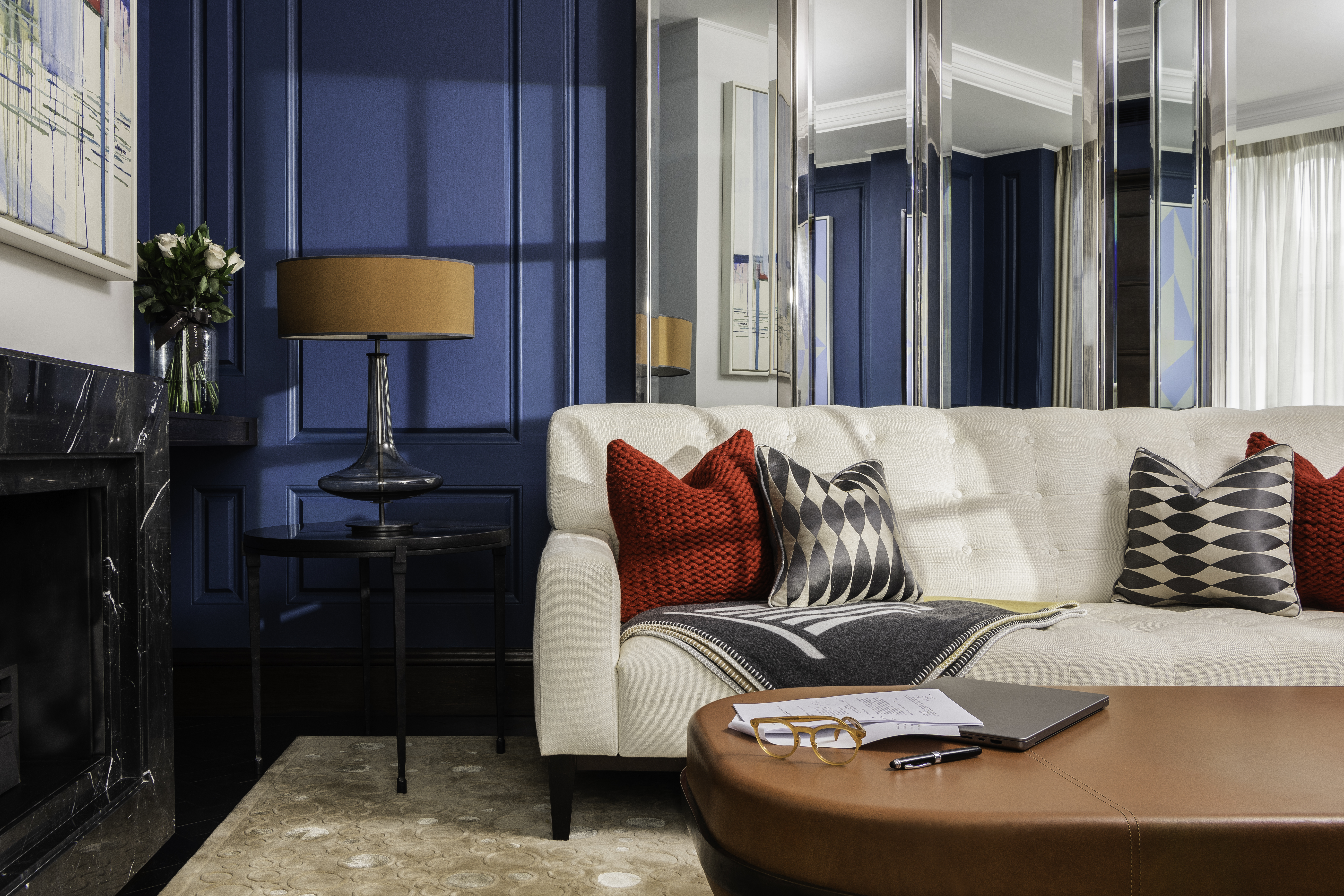 Penthouse suite living area at Corinthia London luxury hotel featuring red and black cushions large sofa and window overlooking London cityscape