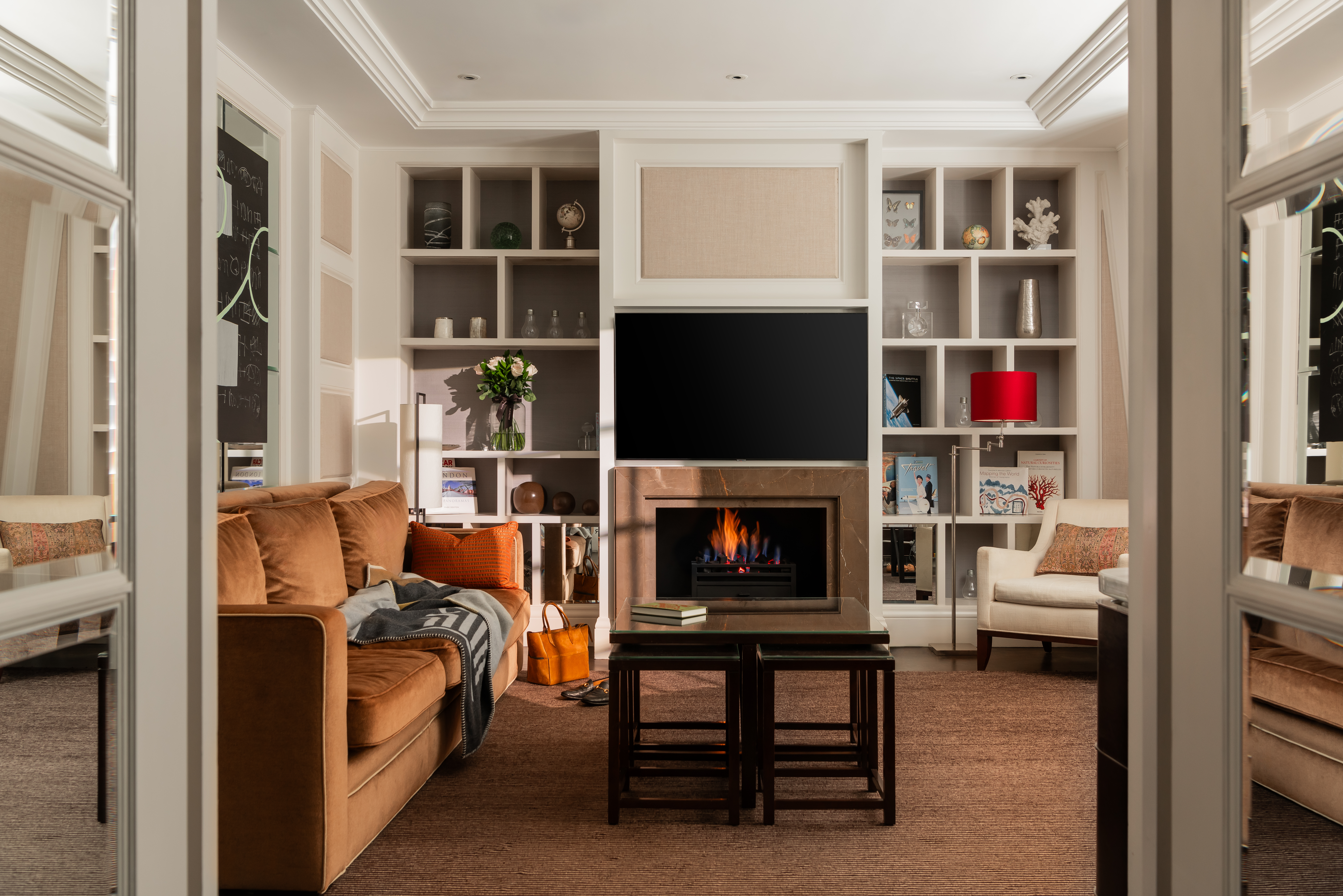 Penthouse suite living area at Corinthia London luxury hotel featuring large TV roaring fireplace and amenities overlooking bay windows with city views