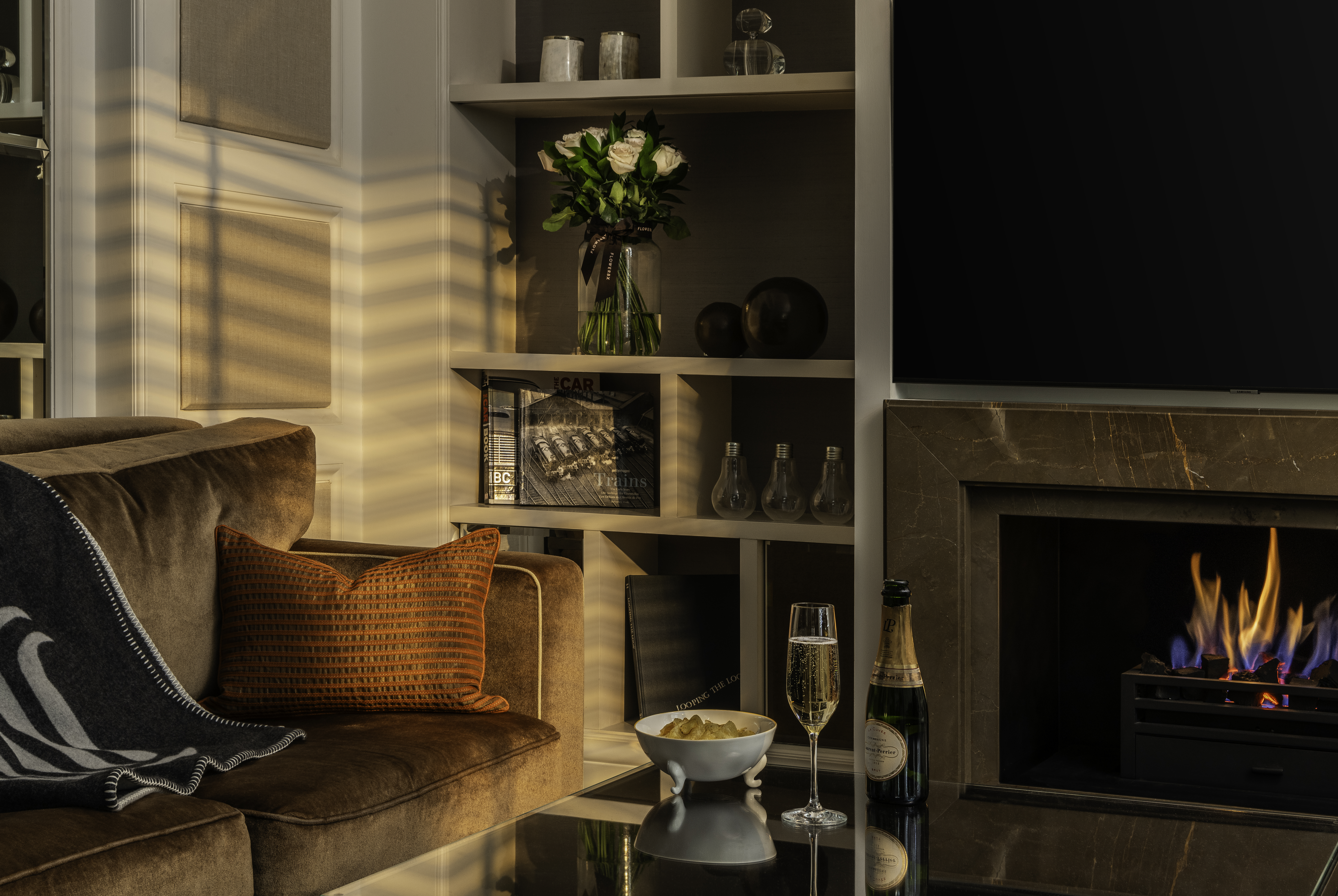 Explorer Penthouse suite living room at Corinthia London luxury hotel near Westminster featuring roaring fireplace bookshelf and glass of Laurent-Perrier champagne with crisps
