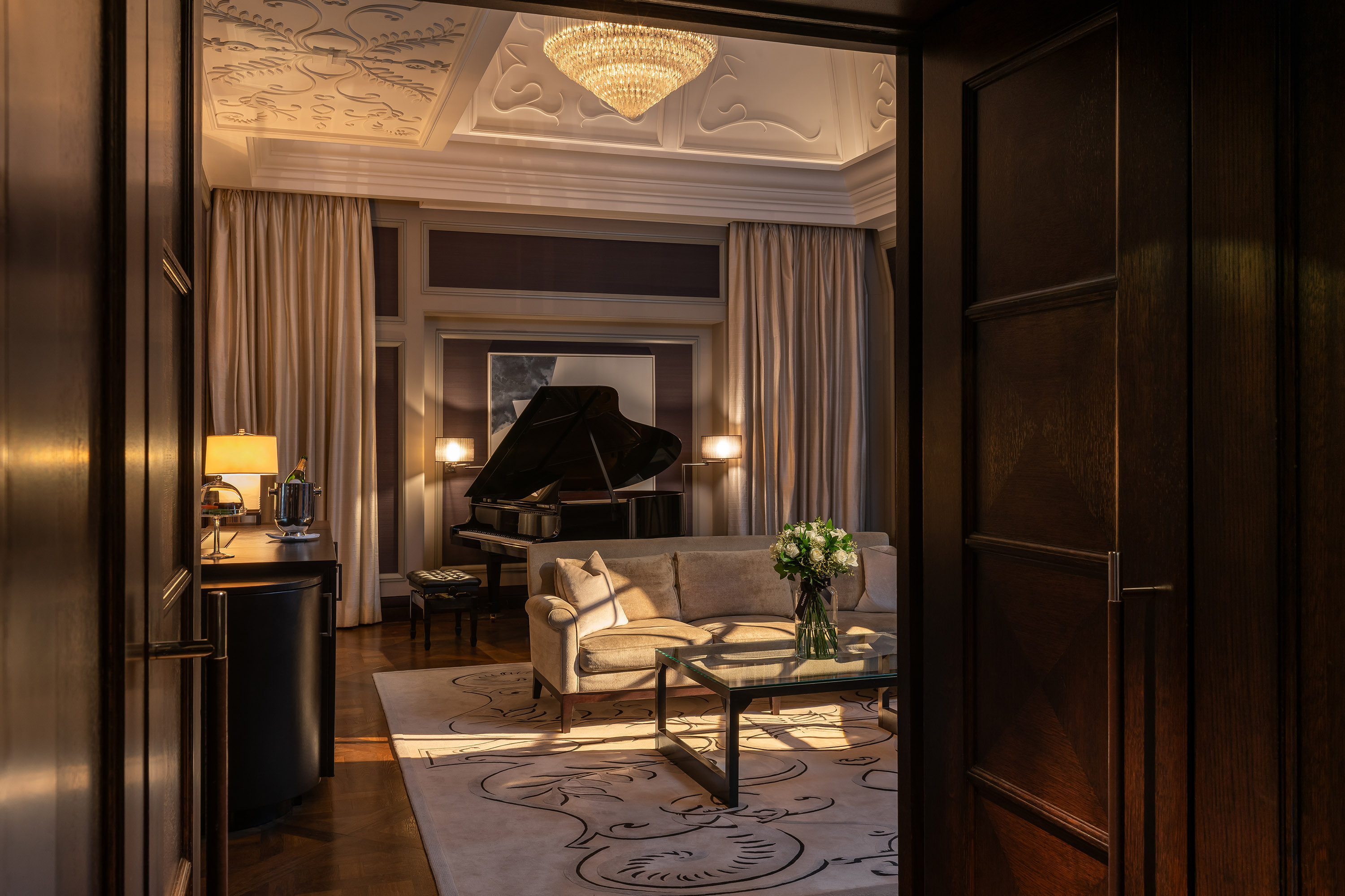 Living area of Musician's Penthouse at Corinthia London luxury hotel near Trafalgar Square featuring large sofa piano and fresh flowers at sunset