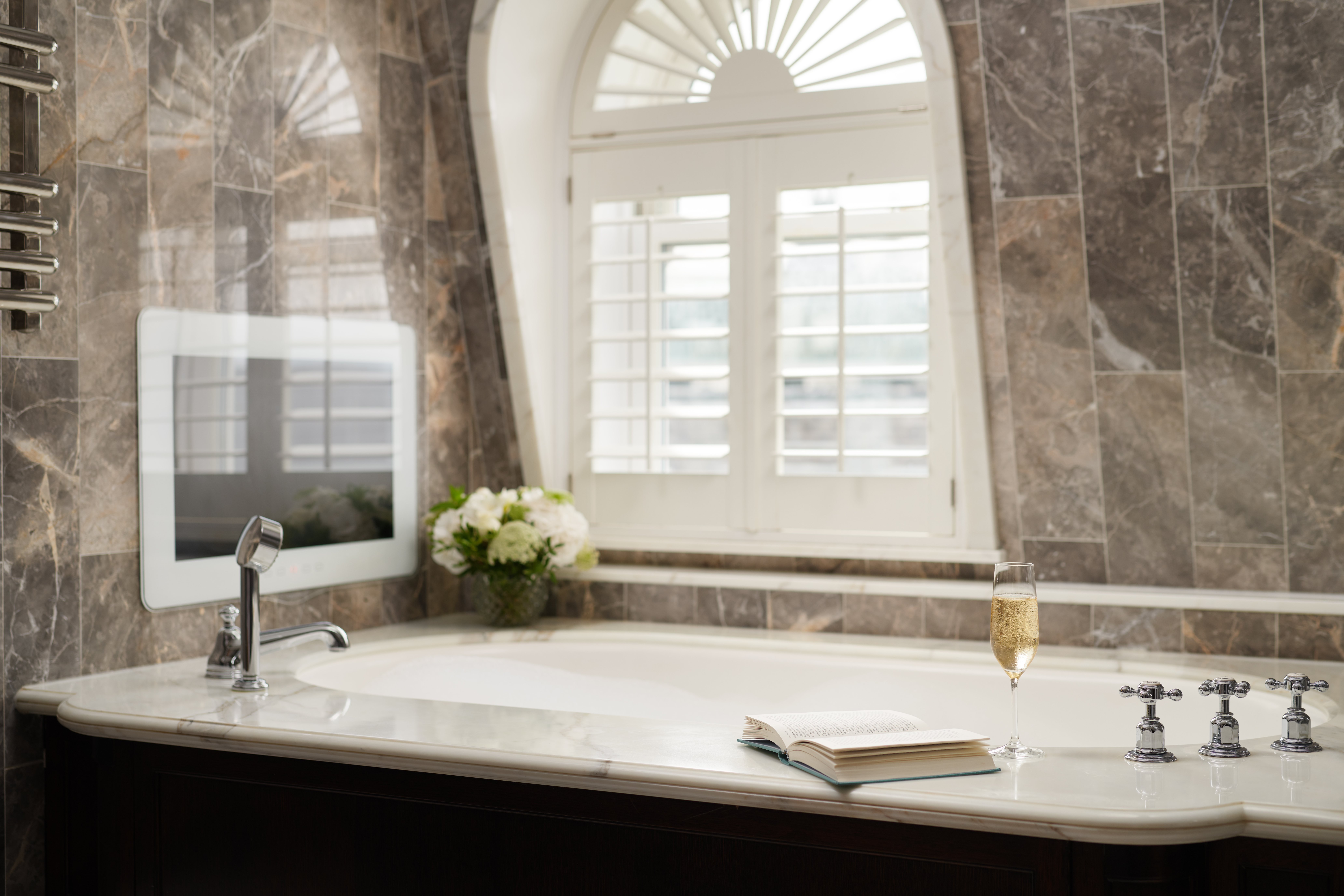 Penthouse suite bathroom at Corinthia London luxury hotel featuring large marble tub TV glass of champagne and book