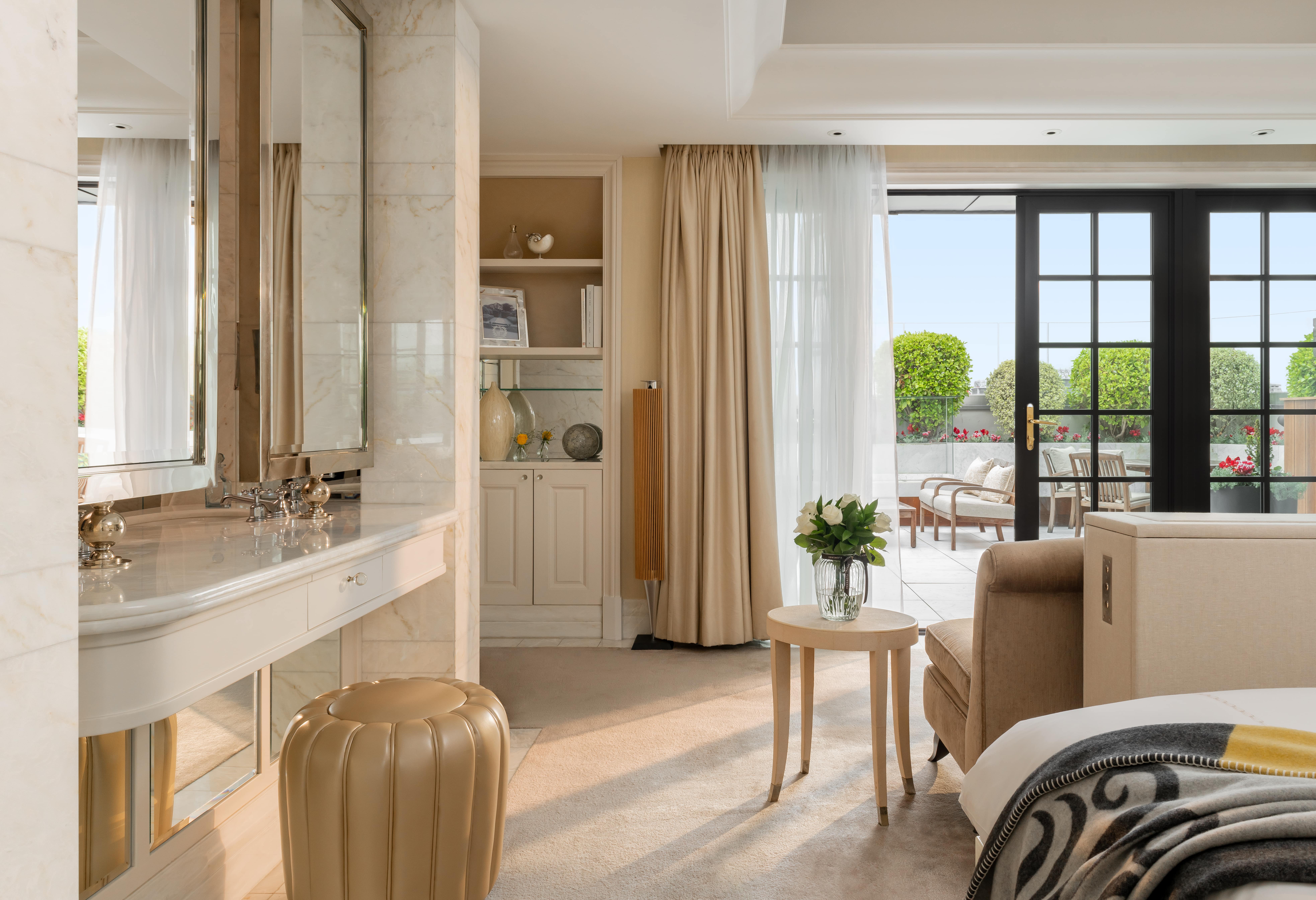 Penthouse suite bedroom at Corinthia London luxury hotel featuring open windows with stunning city views and a stylish makeup table beside the bed.