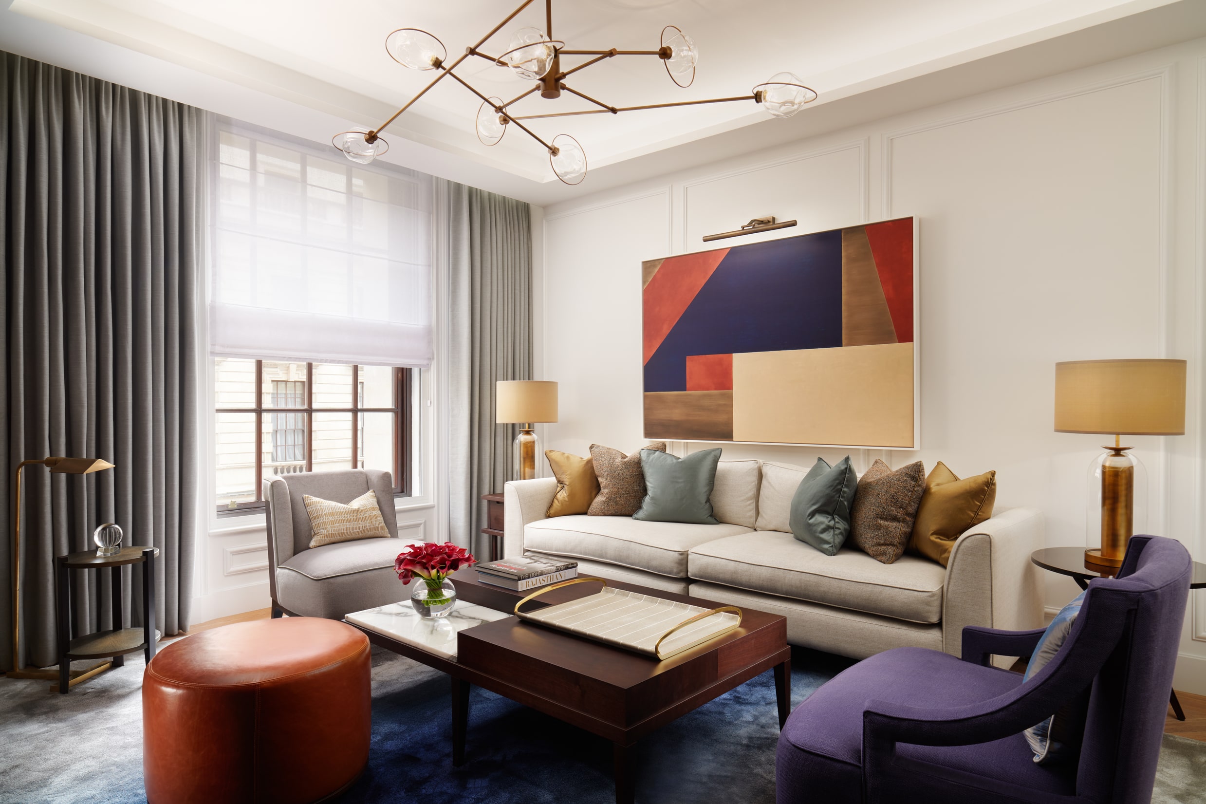 Living room of the London Suite at Corinthia London featuring two elegant chairs, a large sofa, contemporary artwork on the walls and a window overlooking the city.