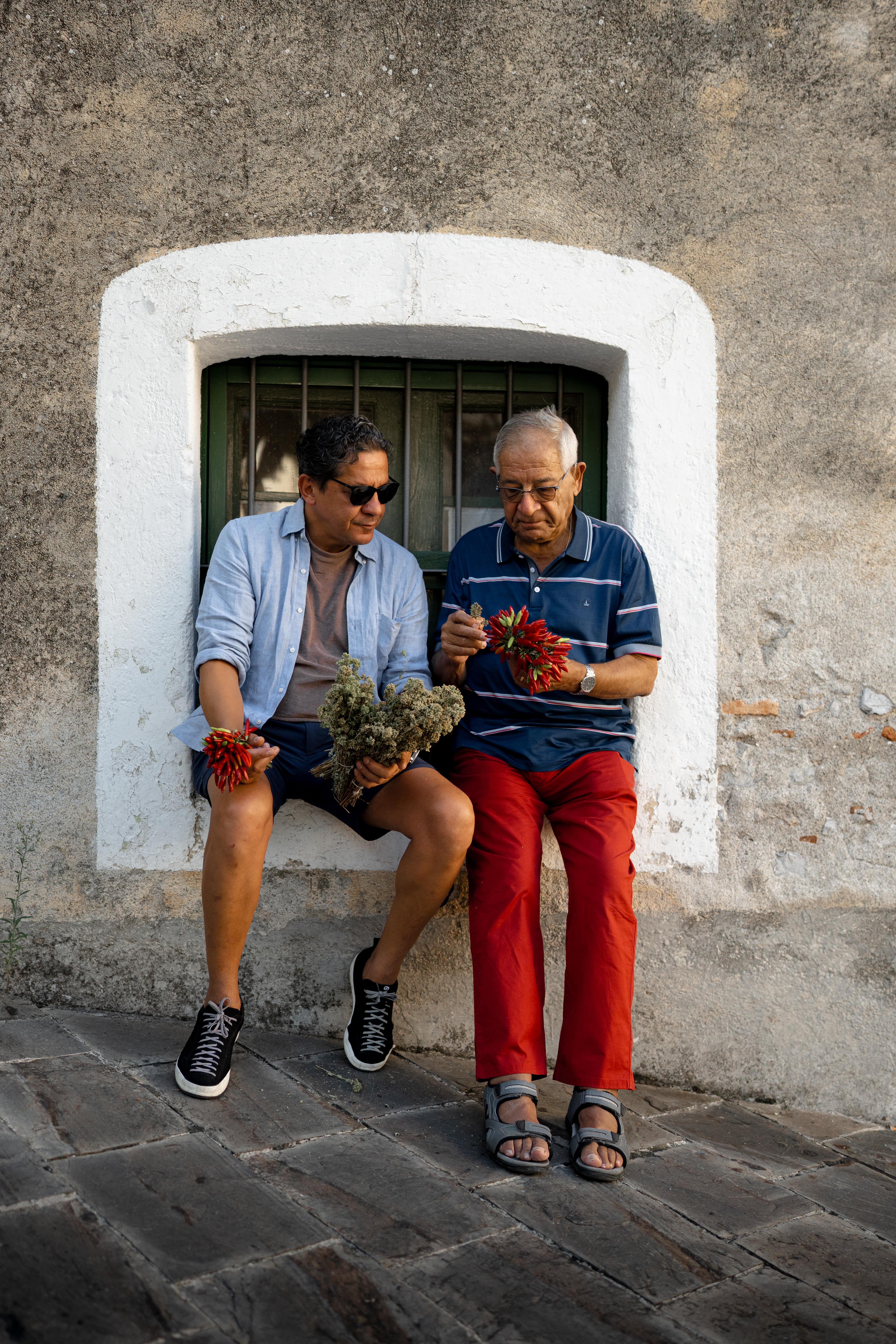 Two people seated outside an Italian building, preparing herbs and peppers, reflecting the culinary heritage behind Mezzogiorno at Corinthia London