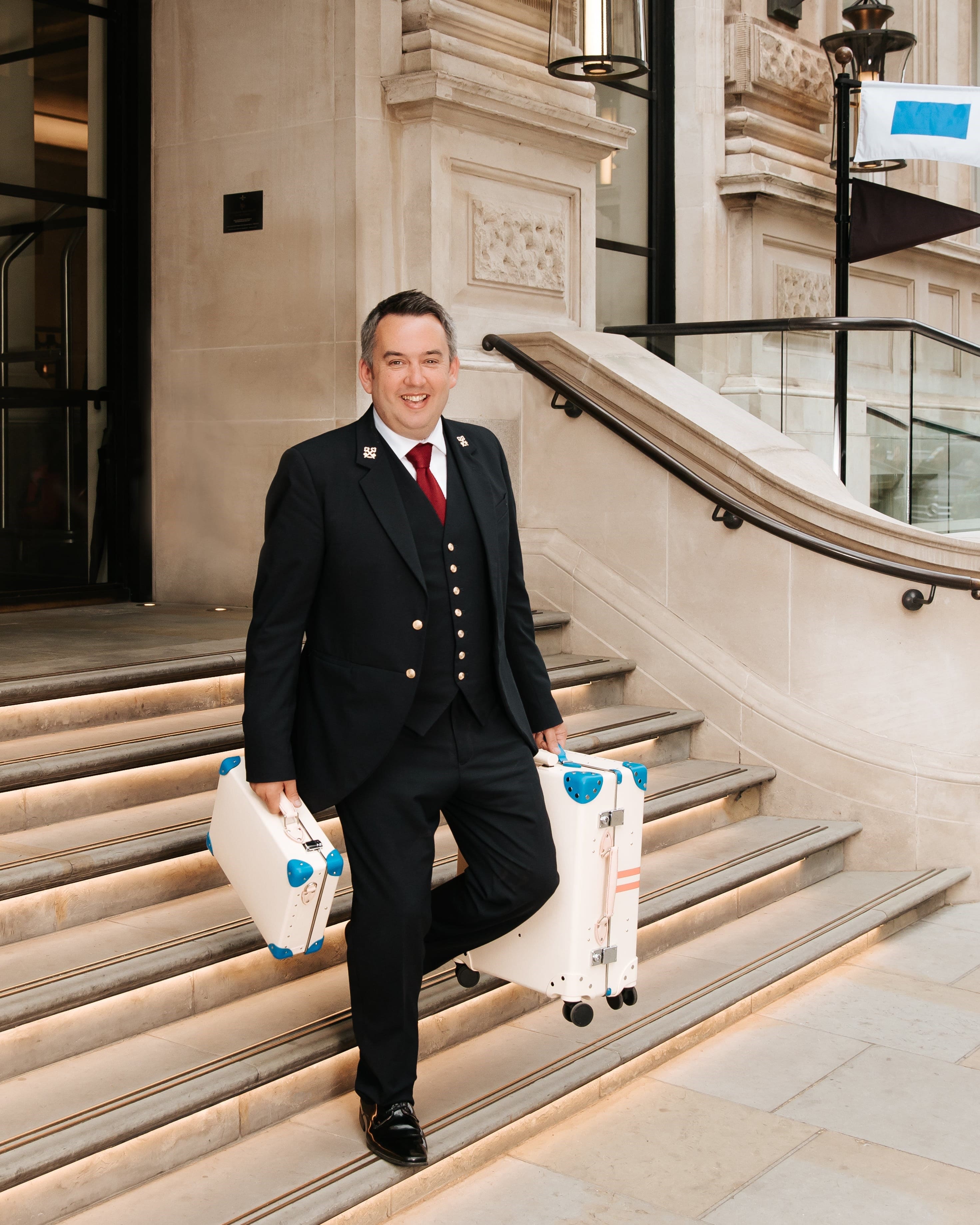 Man taking white luggage down hotel exterior steps
