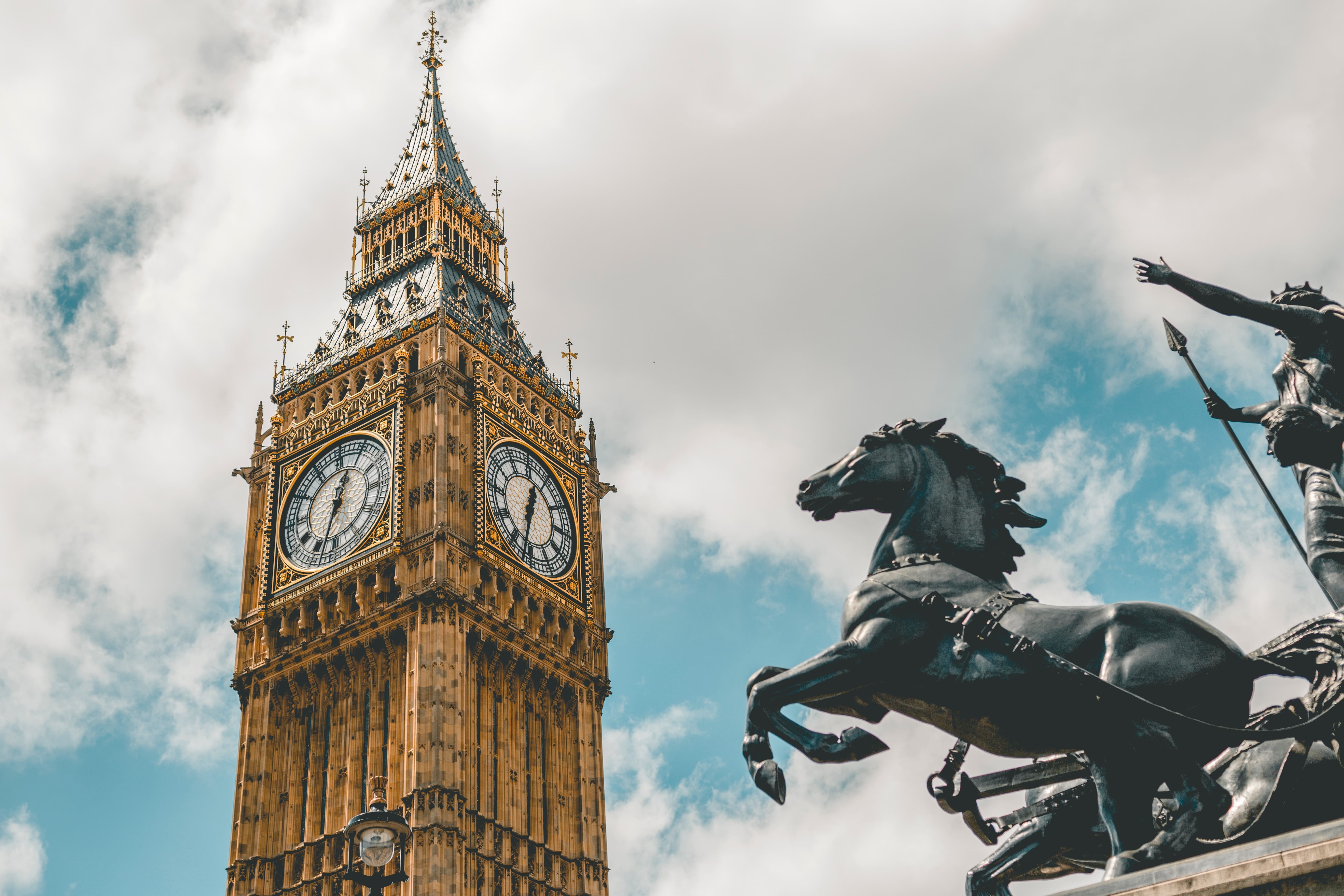 Big Ben and horse statue against a cloudy sky