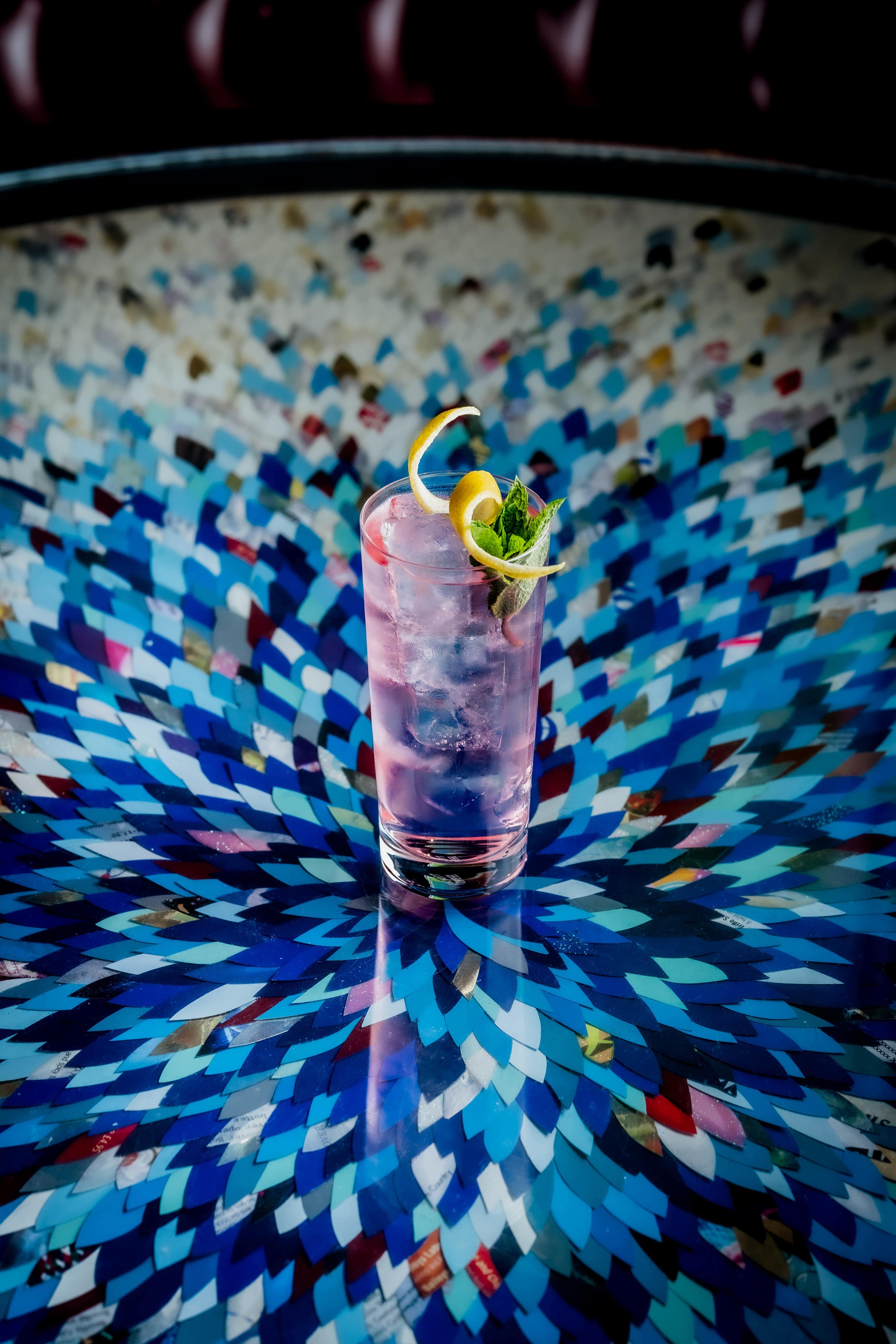 Vesper Tonic cocktail on a glass table with blue artwork underneath 