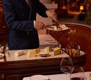 Waiter cutting cheese on a cheese trolley next to a dining table