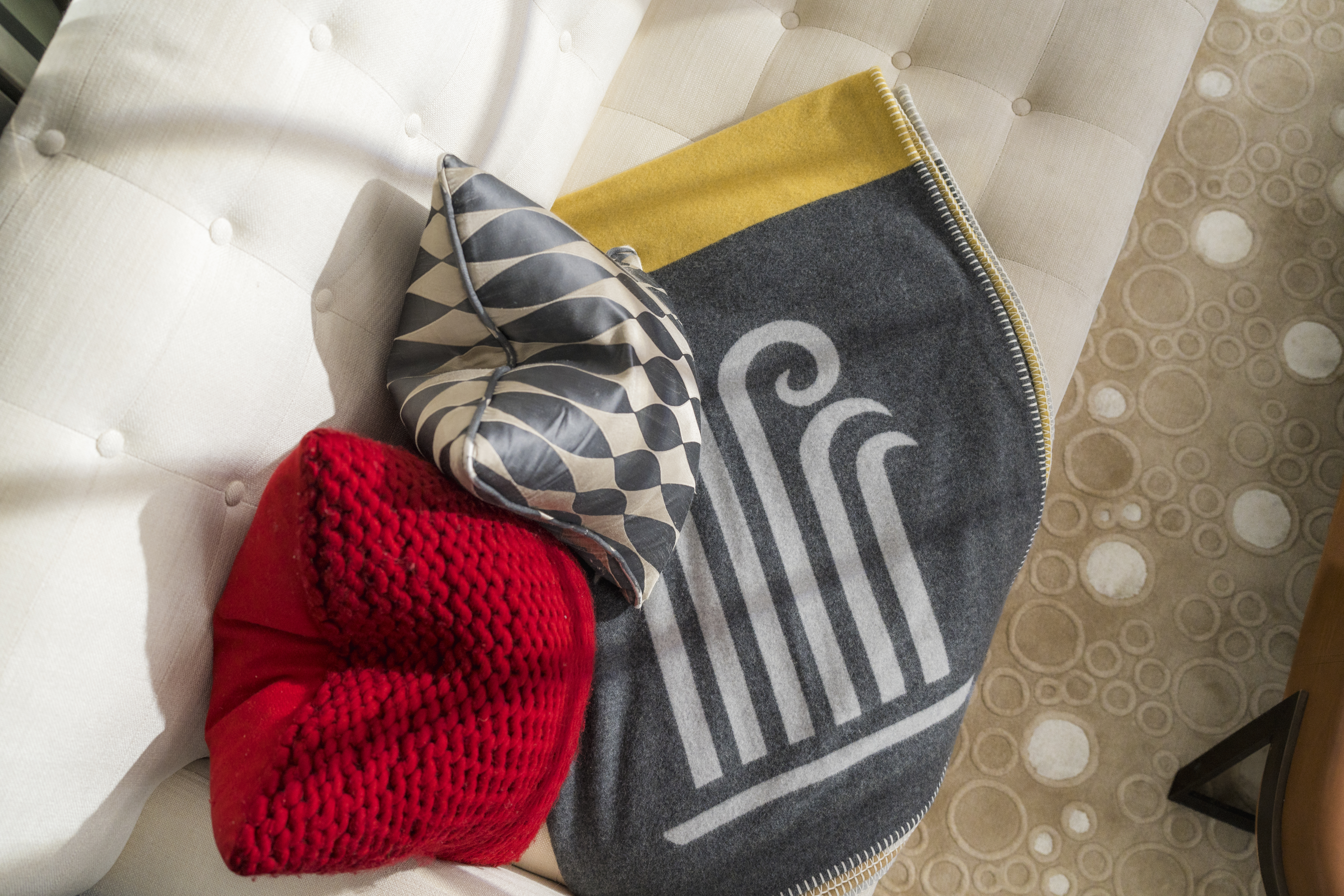 Close-up of living area cushions and Begg x Co cashmere blanket with Corinthia London logo at luxury hotel