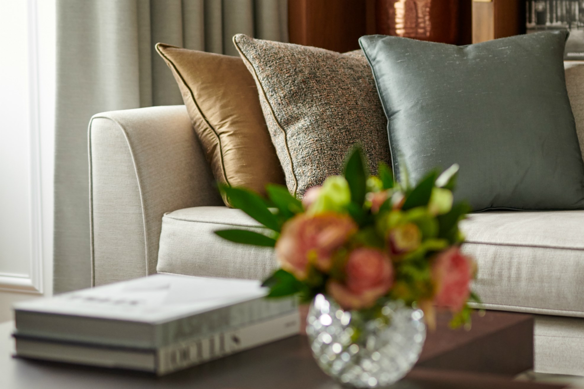 Vase of flowers and books on table next to white sofa with three colourful cushions